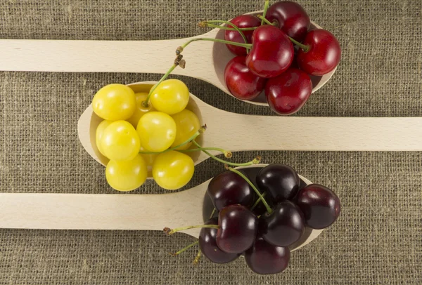 Colorful cherries in a wooden spoon on a natural fabric — 图库照片