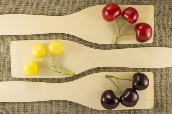 Colorful cherries in a wooden spatula on a natural fabric — ストック写真