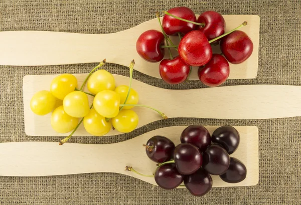 Colorful cherries in a wooden spatula on a natural fabric — Zdjęcie stockowe