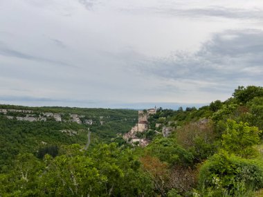 Rocamadour köyü, Fransa 'nın Occitanie bölgesindeki Alzou Kanyonu' nun yukarısındaki kayalıkların üzerine kurulmuştur. Etrafı bulutlu bahar gökyüzünün altında yemyeşil bitki örtüsüyle çevrilidir.