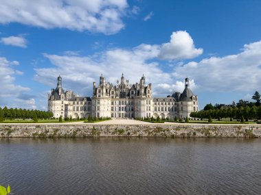 Görkemli Chambord Şatosu, Cosson Nehri 'ne yansıyan, parlak mavi gökyüzünün altında, tüylü beyaz bulutlarla.