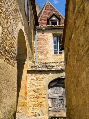 Castelnaud la Chapelle, Dordogne, Fransa 'da dar bir sokak boyunca uzanan taş ve tuğla evlerin geleneksel mimarisi, bir ortaçağ köyünün cazibesini sergiliyor.