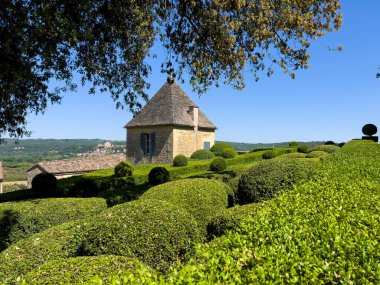 Chateau de Marqueyssac 'daki ağaç bahçelerinin manzarası. Geleneksel bir taş ek binası var. Fransız peyzaj tasarımı sergileniyor.