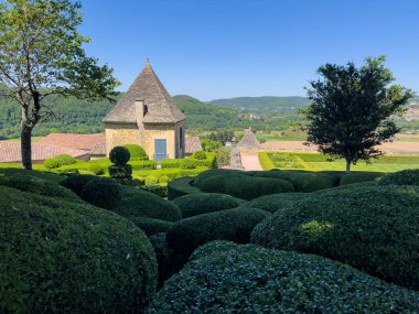 Titizlikle manikürlü Marqueyssac bahçelerinin manzarası. Ağaç, patika ve güneş ışığıyla yıkanmış büyüleyici bir taş bina.