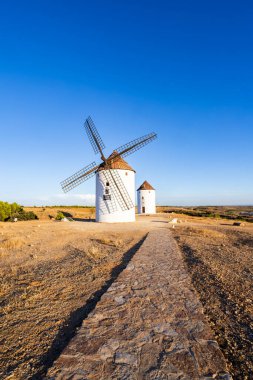Geleneksel La Mancha yel değirmenleri açık mavi gökyüzünün altında kuru bir tepede duruyor.