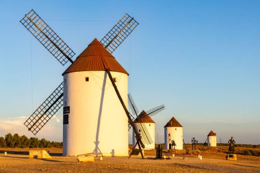 Gün batımında Don Kişot ve Sanço Panza heykelleriyle tepede duran yel değirmenleri.