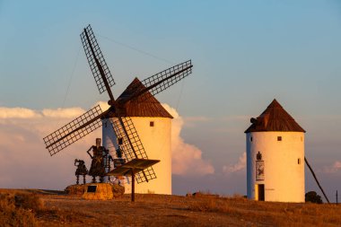 Gün batımında Don Kişot ve Sancho Panza 'nın heykeliyle birlikte iki tarihi İspanyol yel değirmeni.