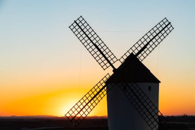 Geleneksel İspanyol yel değirmeni rengarenk bir günbatımı gökyüzüne karşı, tarihi ve seyahati temsil ediyor.