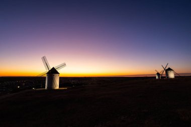 Renkli bir günbatımında Mota del Cuervo 'ya bakan tepelerde duran yel değirmenleri