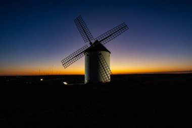 İspanyol yel değirmeni canlı bir alacakaranlık gökyüzüne karşı duruyor, manzara kararıyor ve siluete bürünüyor.