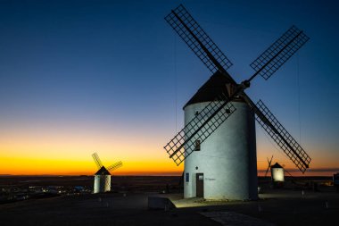 Alacakaranlık sırasında beyaz yel değirmenleri bir İspanyol tepesinde manzarayı noktalıyor.