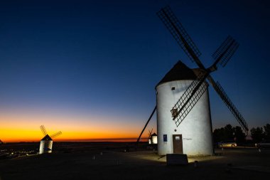 Geleneksel yel değirmenleri, turuncu ve mavi gökyüzüne karşı aydınlatılıyor.