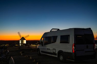 Tepede park etmiş bir karavan ikonik İspanyol yel değirmenine ve renkli La Mancha günbatımına hayran.