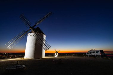 Geleneksel İspanyol yel değirmenleri ve bir karavan La Mancha üzerinde canlı gün batımını yakalıyorlar.