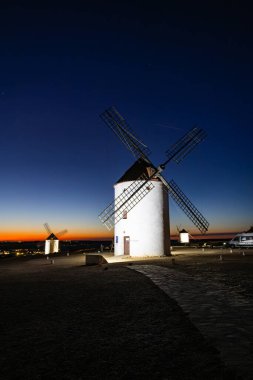 Yel değirmenleri tepede durur, alacakaranlık gökyüzü ufukta altın parıltısıyla ve ilk yıldızlar görünür