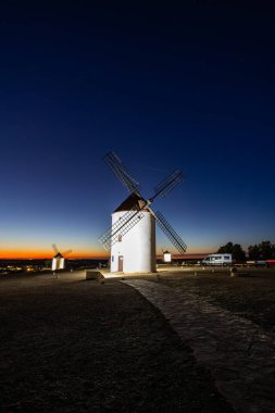 Geleneksel yel değirmenleri alacakaranlıkta Mota del Cuervo, İspanya üzerinde turuncu bir ufuk çiziyor.