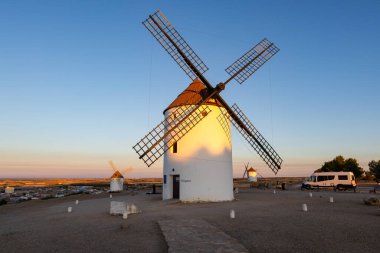 İspanya, Mota del Cuervo 'da renkli bir günbatımında bir tepede duran beyaz yel değirmenleri.