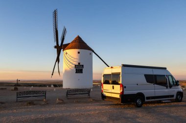 Gün batımında geleneksel İspanyol yel değirmenine hayran olan bir karavan tepede park etmiş.
