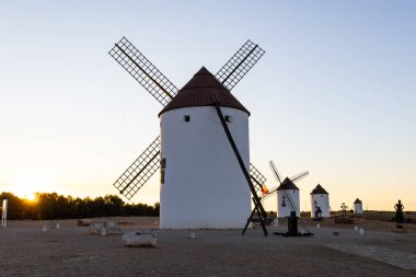Geleneksel İspanyol yel değirmenleri gün batımında bir tepede durup tarihi bir manzarayı sembolize ediyorlar.
