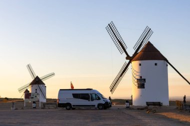 Altın saatinde La Mancha 'da ikonik beyaz yel değirmenlerine hayran olan bir kamp aracı park etti.