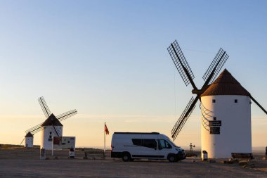 Gün batımında İspanya, Mota del Cuervo 'da ikonik yel değirmenlerinin yanına park edilmiş bir karavan.
