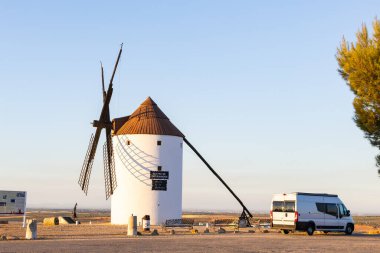 İspanya, La Mancha 'da günbatımında tarihi bir yel değirmeninin yanına park edilmiş bir karavan.