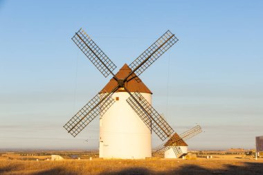 İspanya, La Mancha 'da altın ışığın altında kuru bir arazide duran yel değirmenleri.