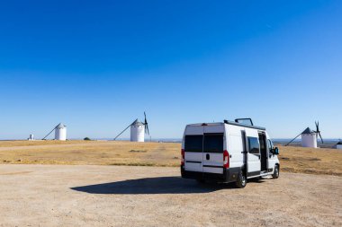 Toprak bir yola park etmiş bir karavan, açık mavi gökyüzü altında özgürlük ve macera yaşıyor.