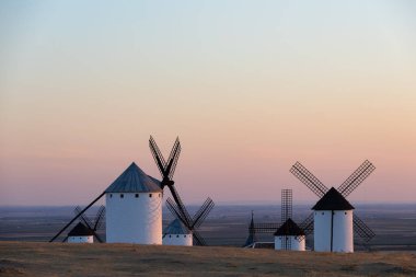 Mancha manzarasının üzerindeki güzel bir günbatımında tarihi yel değirmenleri bir tepenin üzerinde duruyor.