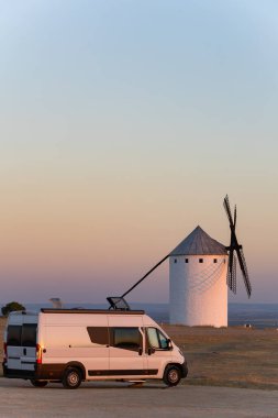 Kamp aracı La Mancha bölgesinde geziyor, renkli gökyüzünün altında ünlü yel değirmenlerini keşfediyor.