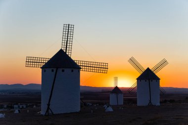 Geleneksel yel değirmenleri, canlı turuncu günbatımı gökyüzüne karşı siluet yaratıyor.