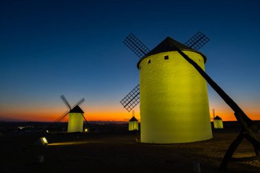 İspanya 'nın Campo de Criptana şehrinde dramatik bir günbatımına karşı yapay ışıkla parlayan tarihi yel değirmenleri
