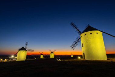 Geleneksel İspanyol yel değirmenleri, Campo de Criptana, La Mancha 'da renkli bir alacakaranlık gökyüzüne karşı aydınlanıyor.