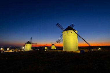 Geleneksel İspanyol yel değirmenleri, La Mancha 'da canlı bir alacakaranlık gökyüzüne karşı aydınlanıyor.