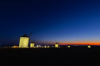 Işıl ışıl yel değirmenleri İspanya 'da canlı bir güneş batımına ve mavi saatli gökyüzüne karşı bir tepenin üzerinde duruyor.