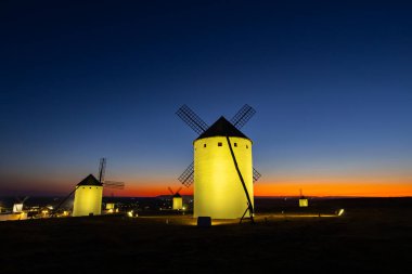 Alacakaranlıkta tepede duran yel değirmenlerinin beyaz yapıları renkli bir gökyüzüne karşı parlıyordu.