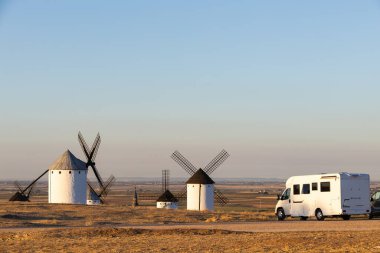İspanya, Campo de Criptana 'daki ikonik yel değirmenlerinin oraya park edilmiş beyaz bir karavan.