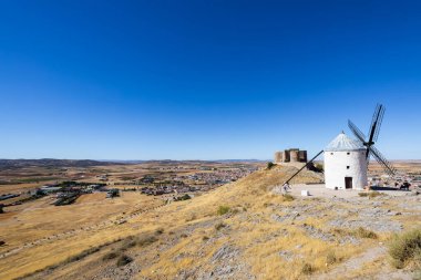 Beyaz yel değirmeni, arka planda bir şato, açık bir günde bir kasabaya bakıyor.