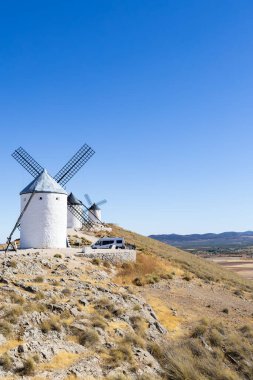 İspanya, Consuegra 'da açık mavi gökyüzünün altında kayalık bir tepede duran beyaz yel değirmenleri.