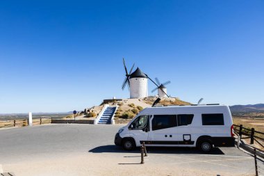 İspanya, Consuegra 'da güneşli bir günde tarihi yel değirmenlerinin yakınına park edilmiş bir karavan.