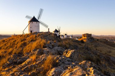 Geleneksel İspanyol yel değirmenleri ve altın saat boyunca tepede duran tarihi bir şato.