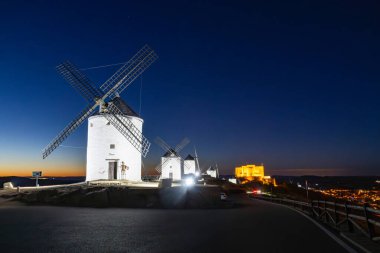 İkonik yel değirmenleri ve İspanya 'nın Consuegra kentindeki koyu mavi gökyüzünün altında aydınlatılmış bir kale.