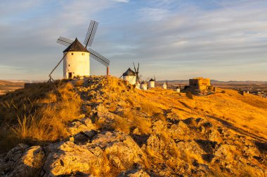 Consuegra yel değirmenleri ve kalesi alacakaranlık gökyüzüne karşı altın bir tepenin üzerinde yıkıldı.