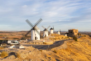 Beyaz yel değirmenleri ve kale bir karavanla tepede duruyor.