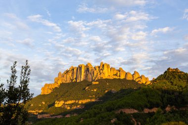 Montserrat dağları belirgin kaya zirveleri ve yemyeşil yamaçlar gün batımında altın ışıkla yıkandı.