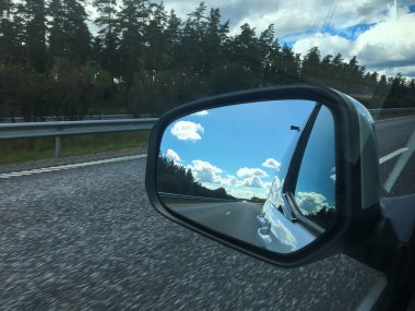 Arabanın yan aynası, Vaggeryd, İsveç 'te bulutlu mavi gökyüzünün altındaki otoyolu yansıtıyor.
