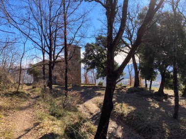 Gökyüzünün altında ağaçlarla çevrili bir yamaçta duran eski taş inziva yeri.