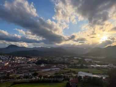 Olot kasabası ve dağlar bulutlu bir gökyüzünün altında ve güneş ışınları altında parlıyor.