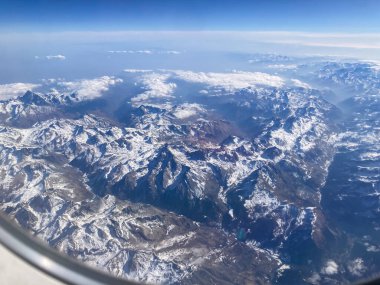 Pireneler karla kaplı dağ zirveleri ve uçak penceresinden görünen bulutlar