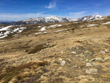 Karlı dağların manzarası ve açık mavi gökyüzünün altındaki kuru bir vadi.